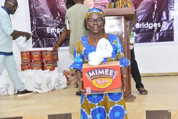 A smiling community member receiving food provisions—including a carton of instant noodles and bagged supplies—during the Prayer of Hannah Foundation empowerment and welfare outreach program.